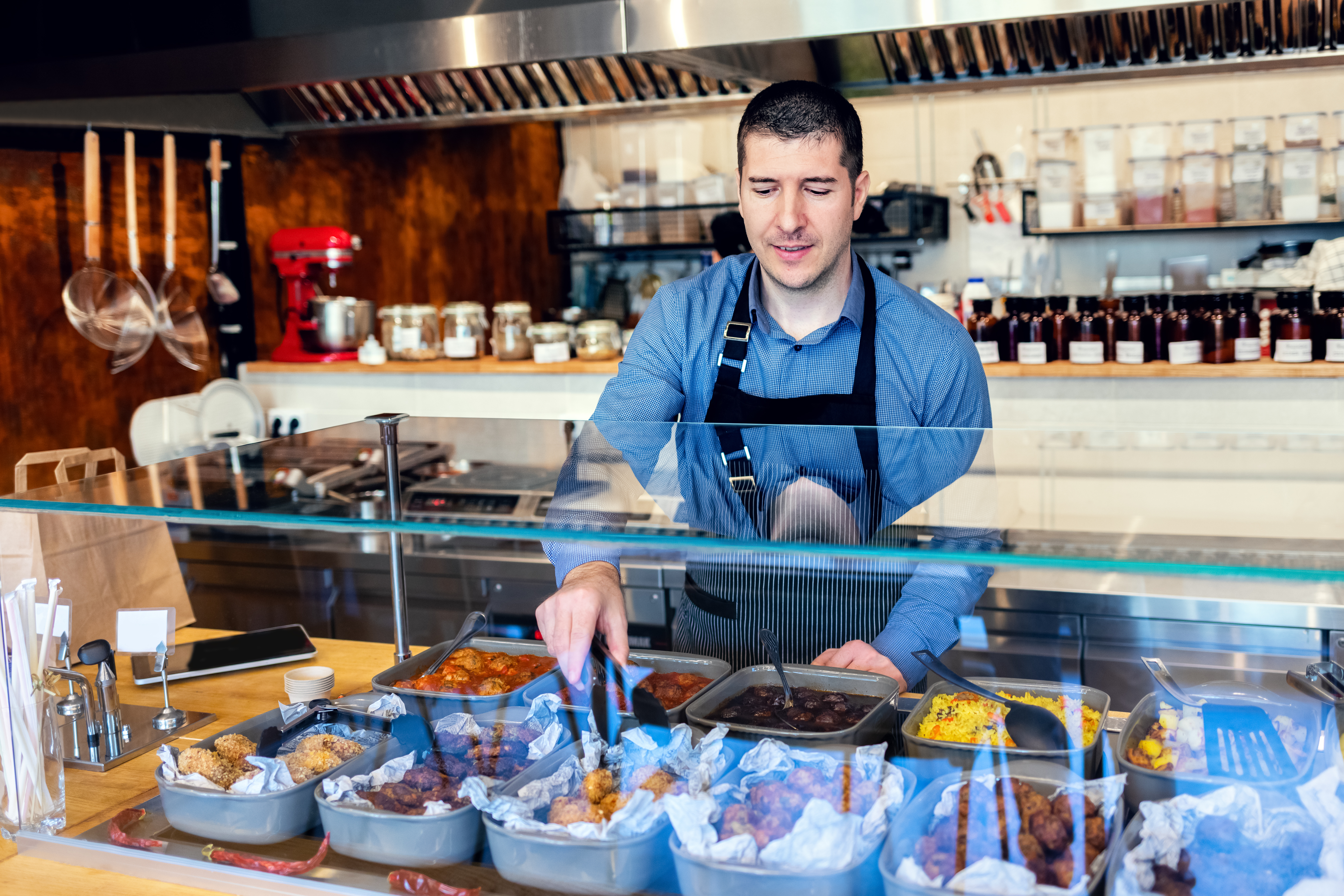 Happy waiter wearing apron serving takeaway food to customer at counter in small family restaurant.